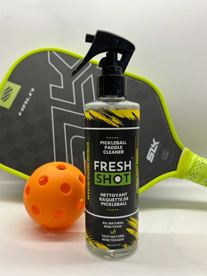 Pickleball paddle cleaner bottle labeled 'Fresh Shot' with an orange pickleball and paddle in the background.