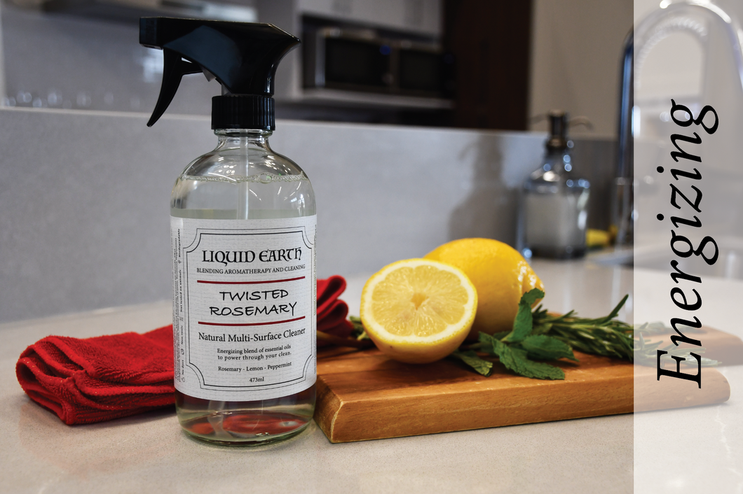 Image of the Twisted Rosemary Natural Multi-Surface Cleaner. The word energizing is used to depict the emotion when using the cleaner. There are lemons, rosemary, a mini wooden cutting board, and a red microfibre cloth in the background.